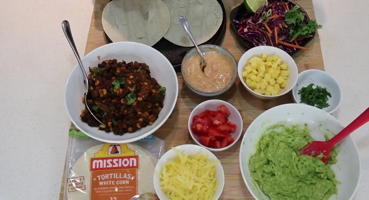 Ingredients for Chipotle Black Bean Tacos laid out on a wooden board, including tortillas, fillings, and toppings.