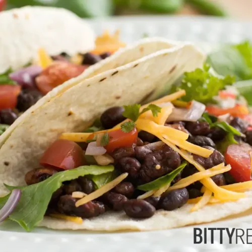 Two completed Chipotle Black Bean Tacos on a white plate, garnished with cheese and vegetables.