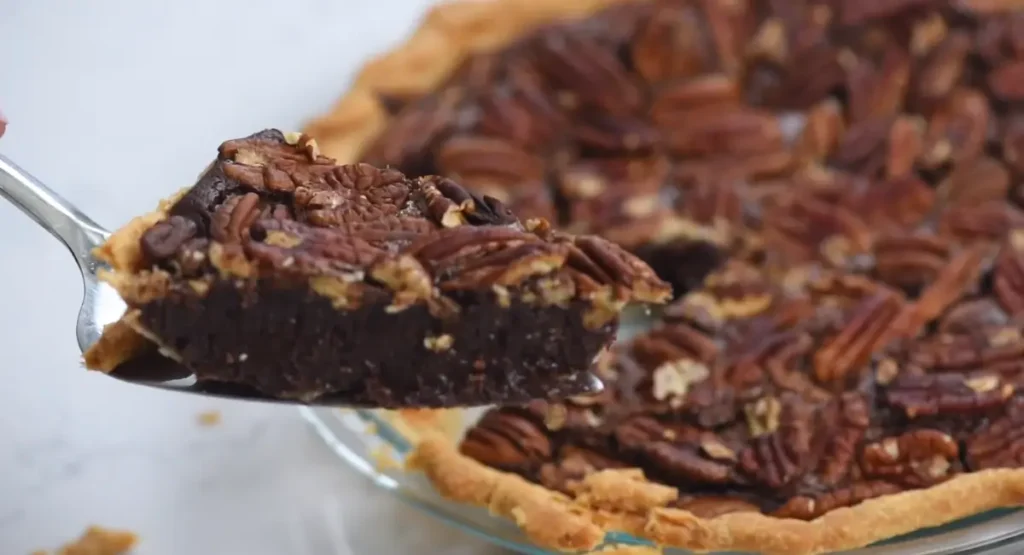 Slice of Chocolate Pecan Pie being lifted from pie plate, showing gooey filling and toasted pecans.