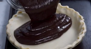 Rich chocolate filling being poured into a pie crust for a Texas Chocolate Pecan Pie.