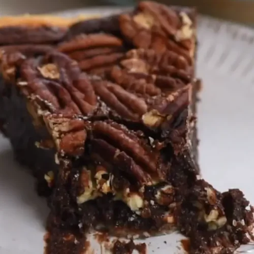 Slice of Texas Chocolate Pecan Pie on a white plate, showing the layers of crust, chocolate filling, and pecans.