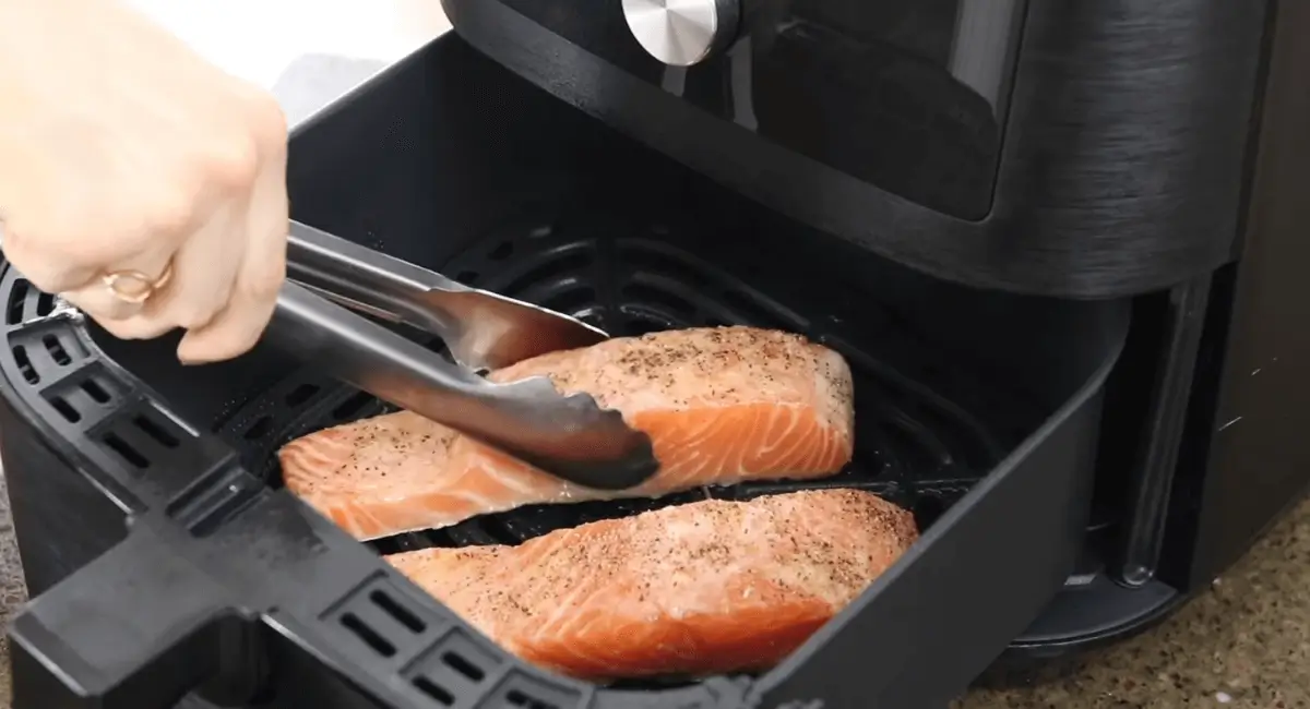 Seasoned frozen salmon fillets being placed in an air fryer basket.