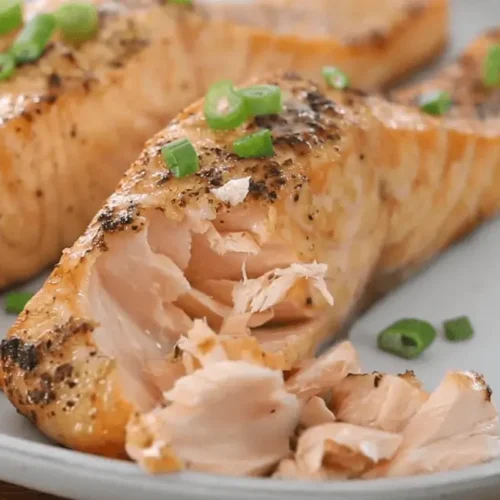 Cooked air fryer frozen salmon, flaky and golden brown, garnished with green onions.