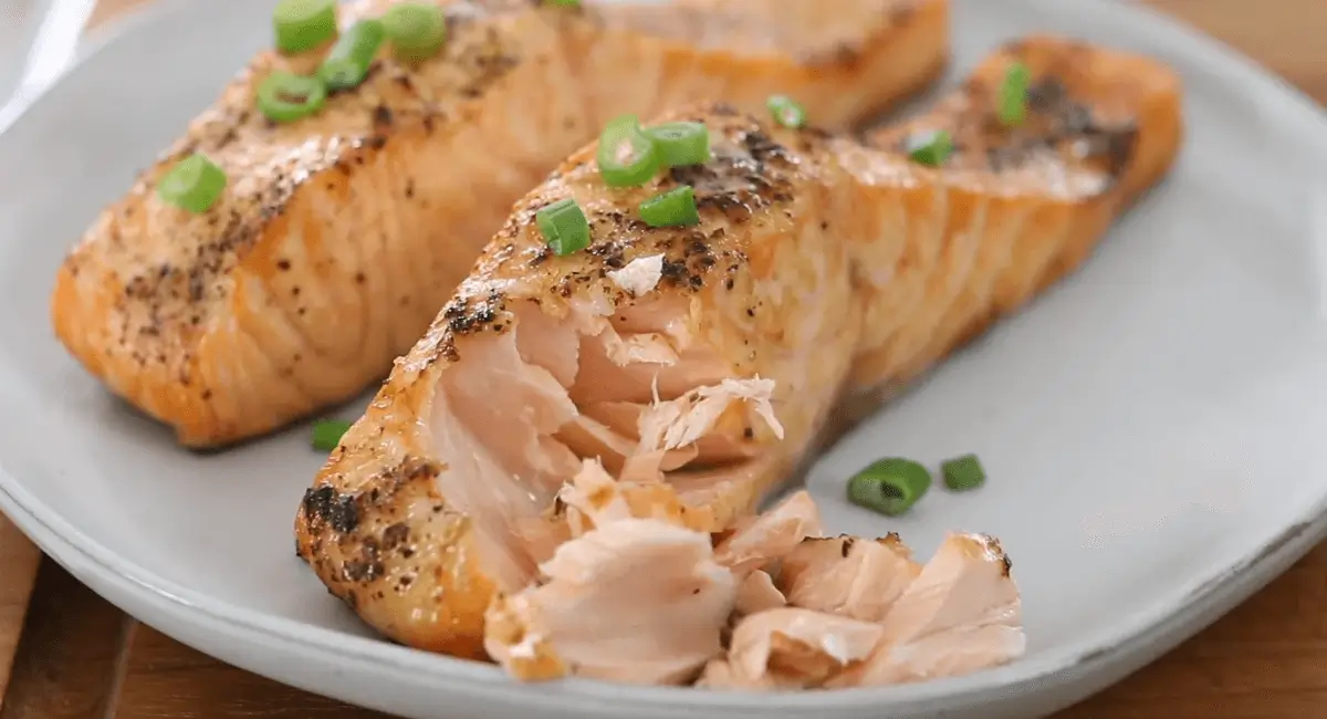 Cooked air fryer frozen salmon, flaky and golden brown, garnished with green onions.