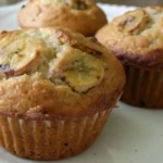 Baked sourdough banana muffins with banana slices on top, on a white plate.
