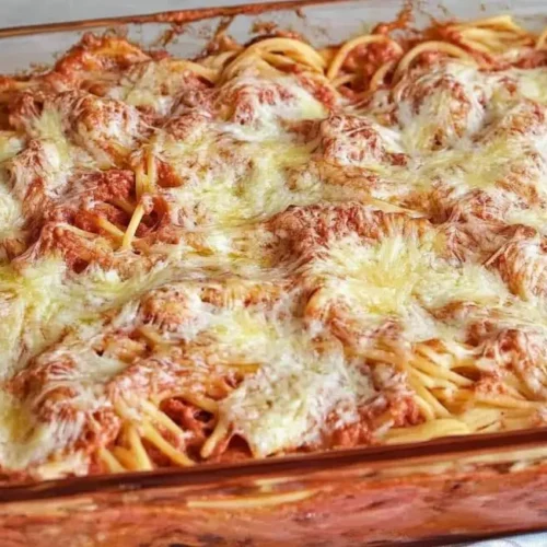 A baked spaghetti casserole in a glass dish, showing melted and slightly browned cheese.