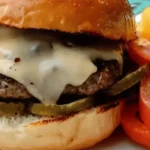 Ultimate Guide to Juicy, Flavorful Venison Burgers 12 A cooked burger with melted white cheese, pickles, and tomatoes on a plate.