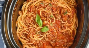 Crockpot spaghetti in a slow cooker, garnished with fresh basil leaves.