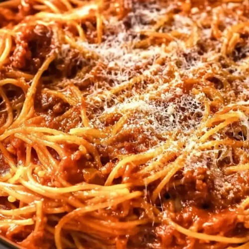 A white bowl overflowing with crockpot spaghetti topped with a sprinkle of grated cheese.