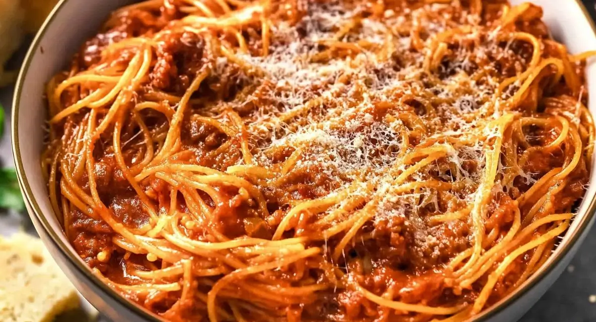A white bowl overflowing with crockpot spaghetti topped with a sprinkle of grated cheese.