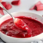 A spoonful of homemade rhubarb sauce lifted from a bowl, demonstrating the texture of the rhubarb sauce recipe.