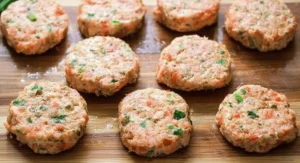 Several uncooked salmon cake patties arranged on a wooden cutting board, ready for cooking as part of a salmon cake recipe.