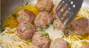 Meatballs and spaghetti are simmering in a pan with sauce.