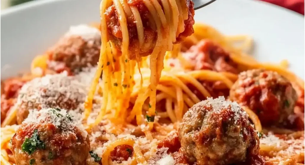 A close-up of a fork twirling spaghetti and meatballs covered in sauce and cheese.