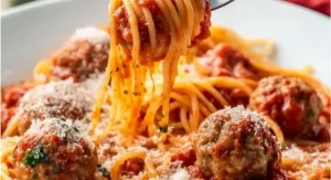 A close-up of a fork twirling spaghetti and meatballs covered in sauce and cheese.