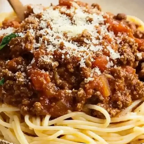 A plate of spaghetti bolognese topped with grated cheese.