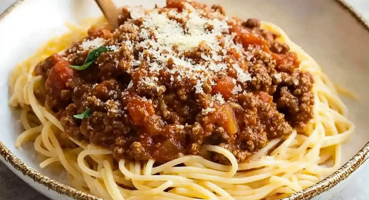 A plate of spaghetti bolognese topped with grated cheese.