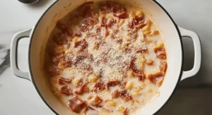 Creamy spaghetti carbonara with chunks of meat and cheese in a white pot.