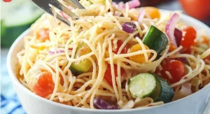 Close-up of a colorful spaghetti salad being lifted with a fork.
