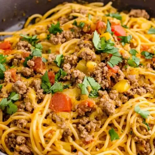 Close-up of a skillet filled with cheesy taco spaghetti, garnished with fresh cilantro.