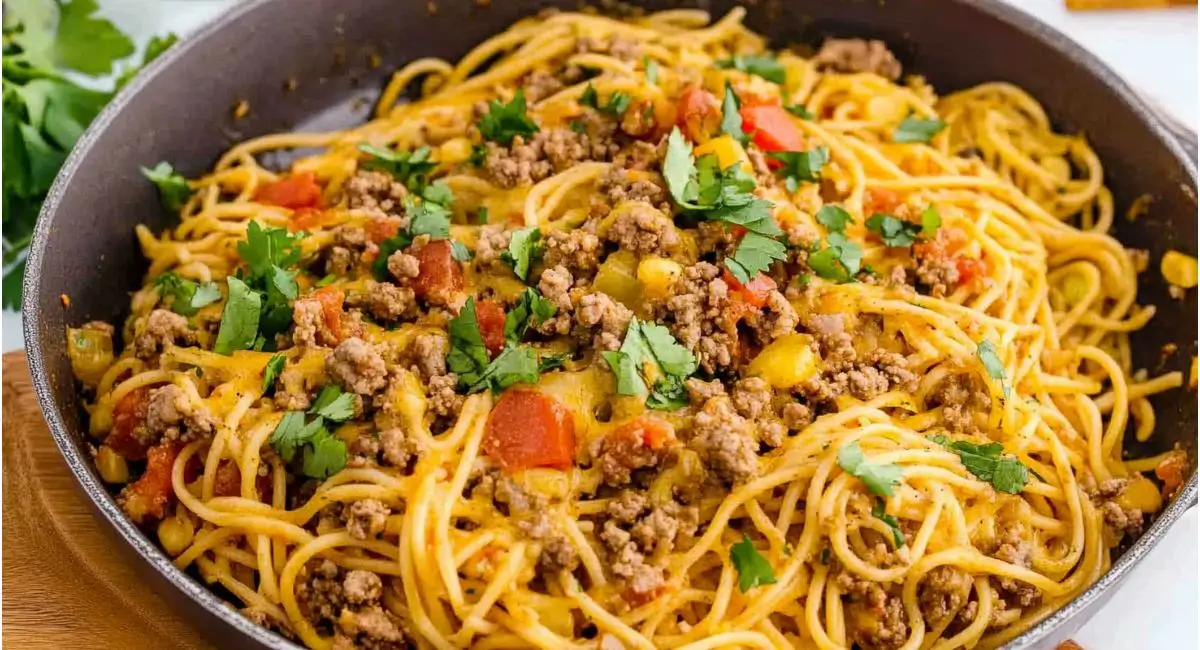 Close-up of a skillet filled with cheesy taco spaghetti, garnished with fresh cilantro.