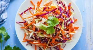 A single serving of colorful Asian Slaw with Sesame Dressing on a white plate, garnished with cilantro.