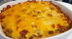 A close-up of a baked Bacon Cheeseburger Casserole in a white oval dish, featuring melted cheddar cheese, ground beef, and bacon pieces.