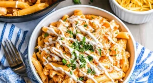 A bowl of creamy Buffalo Chicken Pasta garnished with white sauce and parsley on a blue and white napkin.