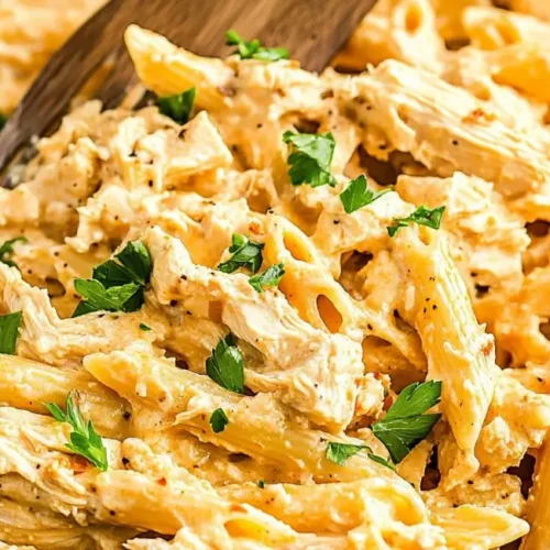 Creamy Buffalo Chicken Pasta in a blue skillet with a wooden utensil, garnished with fresh parsley.