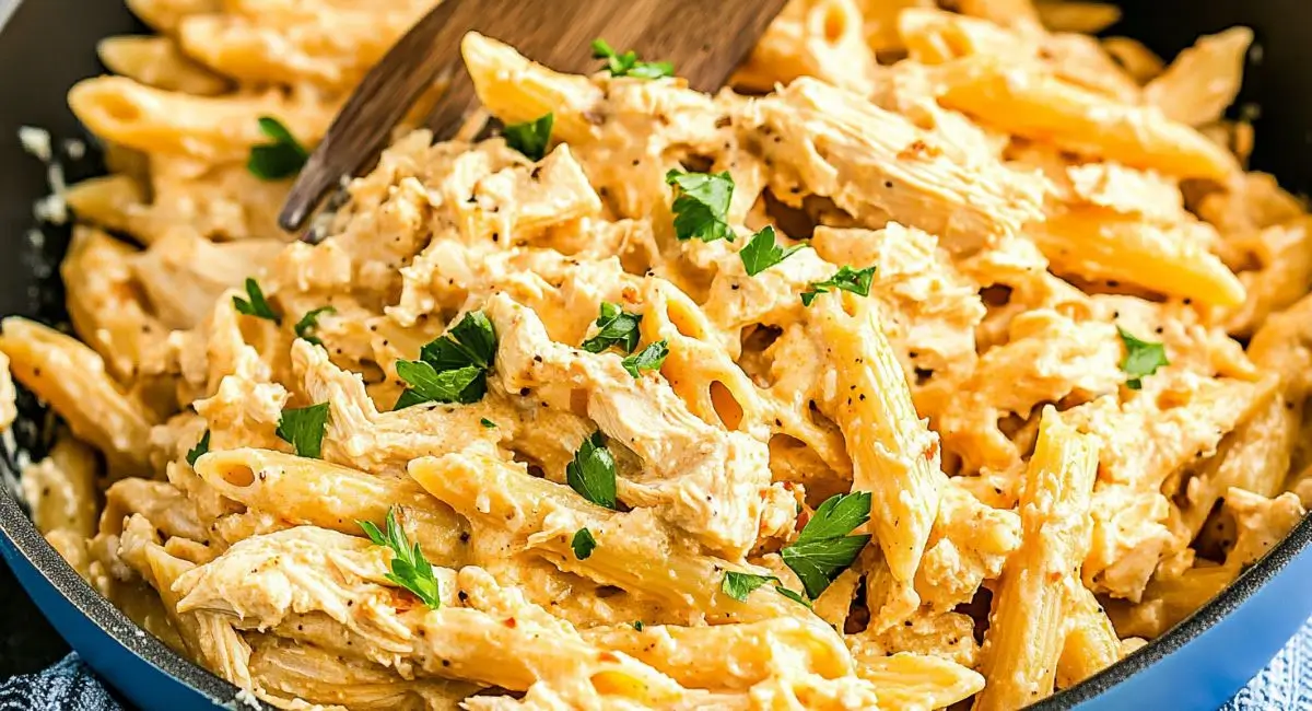 Creamy Buffalo Chicken Pasta in a blue skillet with a wooden utensil, garnished with fresh parsley.