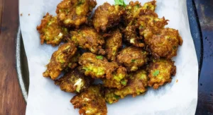 A pile of golden brown Cauliflower Fritters resting on white parchment paper on a dark surface.