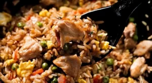 A close-up view of a spoonful of Chicken Fried Rice Recipe, featuring chicken, peas, egg, and other vegetables.