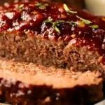 A close-up of a sliced classic meatloaf recipe, generously glazed with a rich, glossy sauce and garnished with fresh thyme sprigs, showcasing its moist interior.