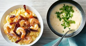 Two bowls of Shrimp and Grits are presented on a light wooden surface, one with whole shrimp and the other with chopped parsley.