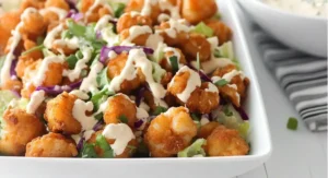 A high-angle view of a white bowl of EASY Popcorn Shrimp Salad with crispy shrimp, greens, purple cabbage, and creamy dressing.