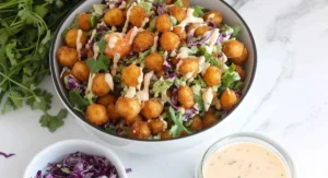 A top-down shot of a round white bowl of EASY Popcorn Shrimp Salad with crispy shrimp, mixed greens, purple cabbage, and creamy dressing, surrounded by ingredients.