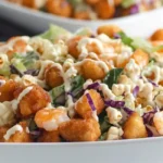 A close-up of a white square bowl filled with EASY Popcorn Shrimp Salad, featuring crispy shrimp, mixed greens, purple cabbage, and a creamy dressing.