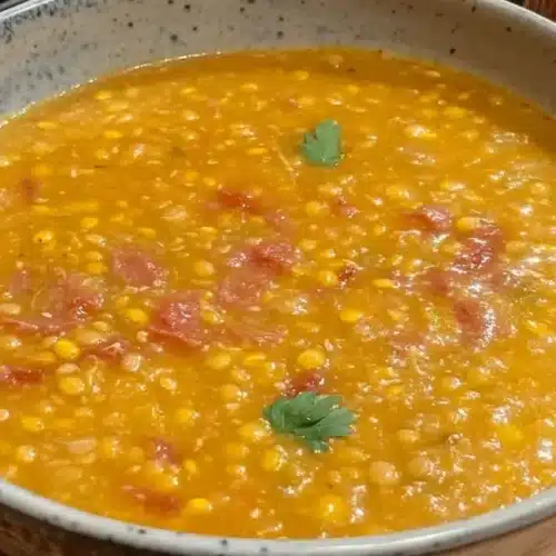 A full bowl of Hearty Scottish Lentil Soup: A Wholesome Comfort Classic, garnished with fresh parsley, sits on a wooden surface next to slices of bread.