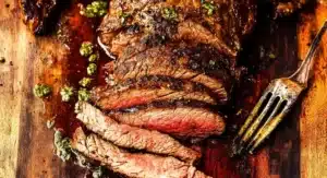 Sliced and seasoned juicy flank steak on a wooden board with green sauce and a fork. Juicy Flank Steak Recipe.