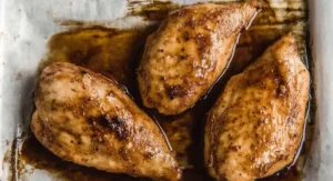 Three golden-brown baked chicken breasts resting on a piece of parchment paper on a baking sheet, glistening with the remnants of the Korean Chicken Marinade.