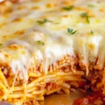Close-up of a slice of layered Spaghetti Pie being removed from a round foil pan, showcasing the spaghetti, meat sauce, and melted cheese layers.