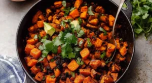 A cast iron skillet filled with hearty Tex-Mex Sweet Potato Hash, garnished with cilantro and avocado.