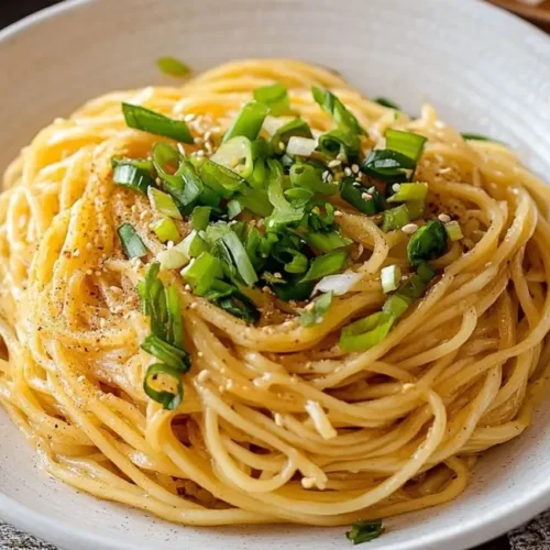 An overhead shot of a light-colored bowl brimming with Vietnamese Garlic Noodles, generously garnished with vibrant green scallions and sesame seeds, resting on a patterned napkin with chopsticks to the right.