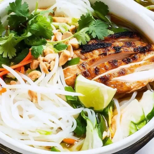 A white bowl of Vietnamese Noodle Bowl with Chicken topped with grilled chicken, herbs, vegetables, a lime wedge, and chopsticks.