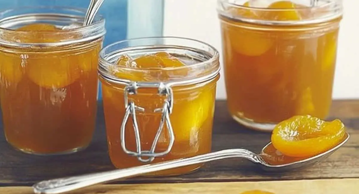 Three jars of preserved apricots with a spoonful of the fruit in front, representing a delicious outcome of a dry apricot recipe.