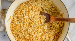 A top-down view of a wooden spoon stirring a pot full of cooked fluffy rice pilaf.