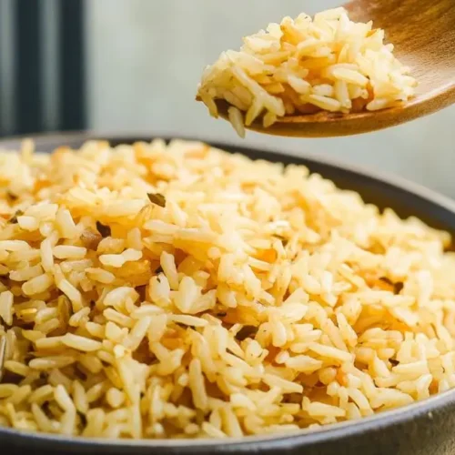 A close-up shows a spoonful of fluffy rice pilaf held above a bowl filled with the same golden-brown rice dish.