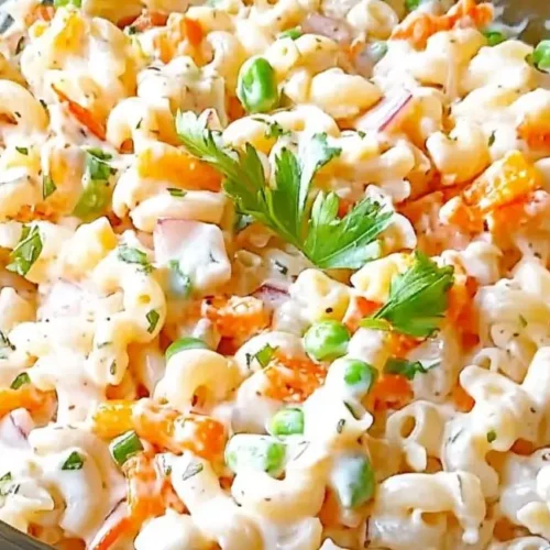 A clear glass bowl filled with creamy macaroni salad containing diced carrots, peas, and red onions, a colorful interpretation of the Hawaiian pasta salad recipe.