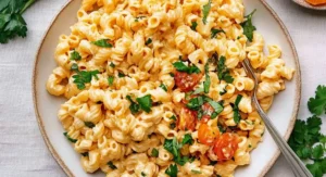 A plate of creamy macaroni salad with halved cherry tomatoes and fresh parsley, a variation of the Hawaiian pasta salad recipe.