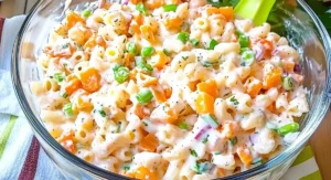 A clear glass bowl of creamy macaroni salad with diced carrots, peas, and green onions, a refreshing example of the Hawaiian pasta salad recipe.